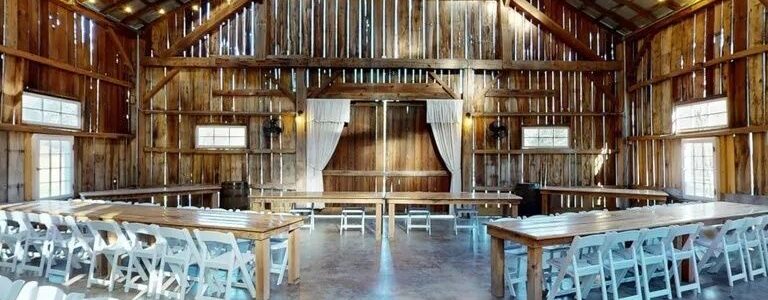 Rustic barn event hall with high ceiling, wood walls, and folding tables