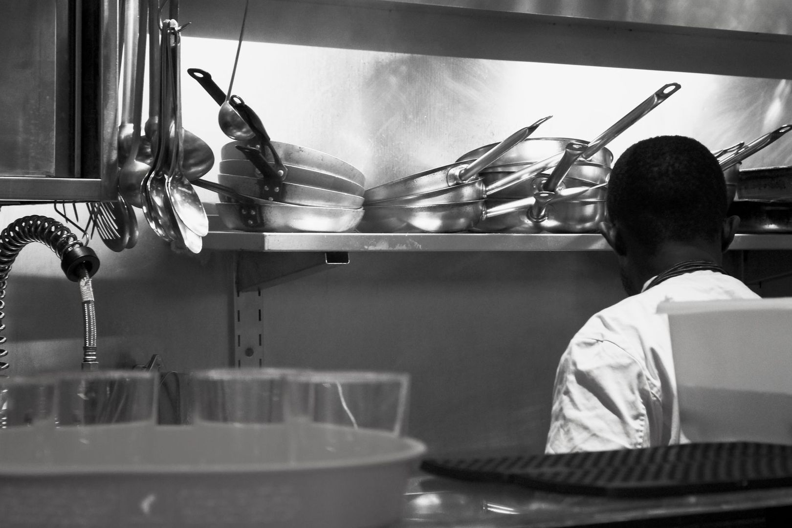 Commercial kitchen worker beside shelves of pans and cooking utensils